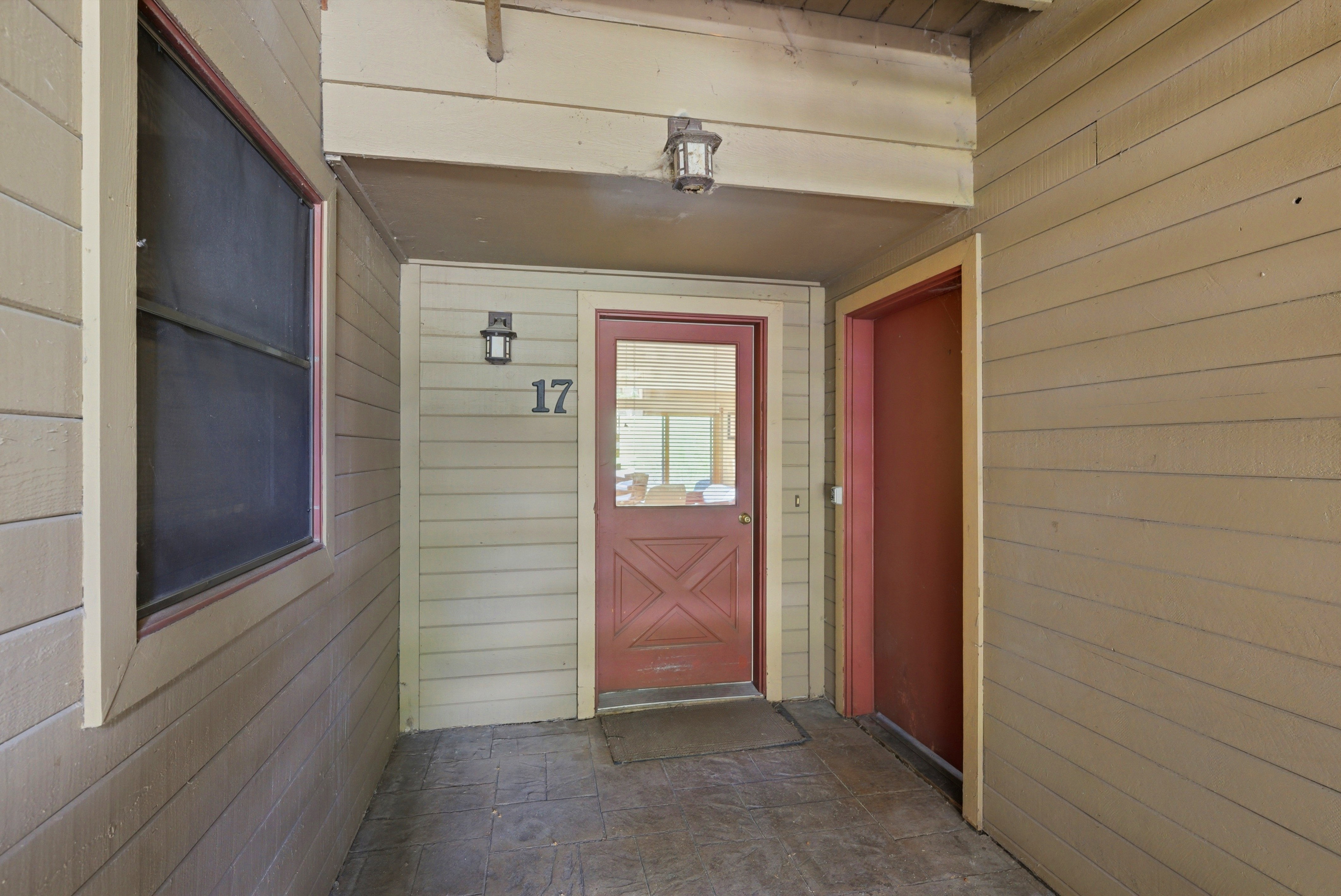 Entryway featuring a glass-paneled door with a decorative kick plate, exterior wall sconces, and house number 17