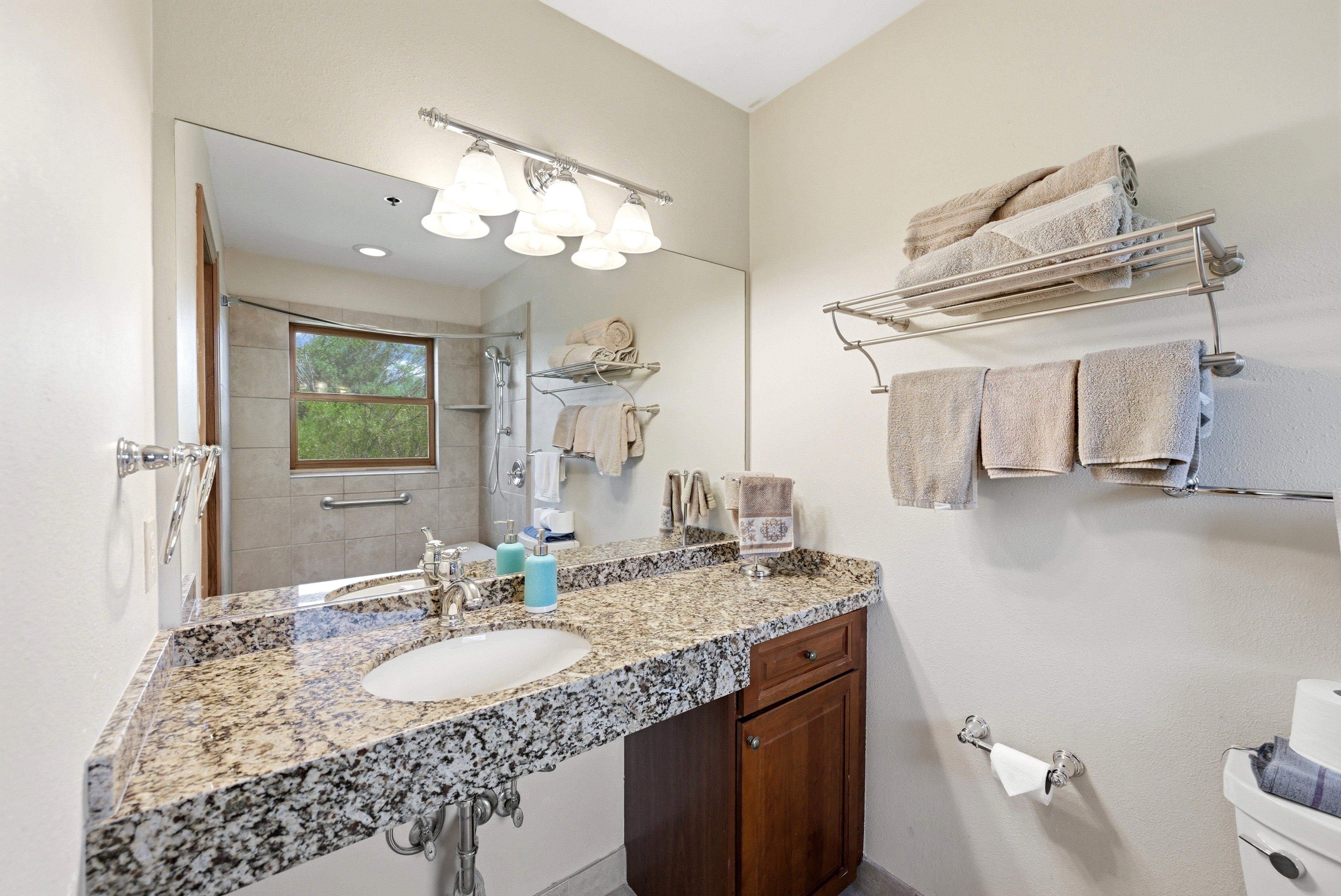 Spacious vanity featuring a granite countertop with an undermount sink, ample storage cabinetry, and a large wall-mounted mirror