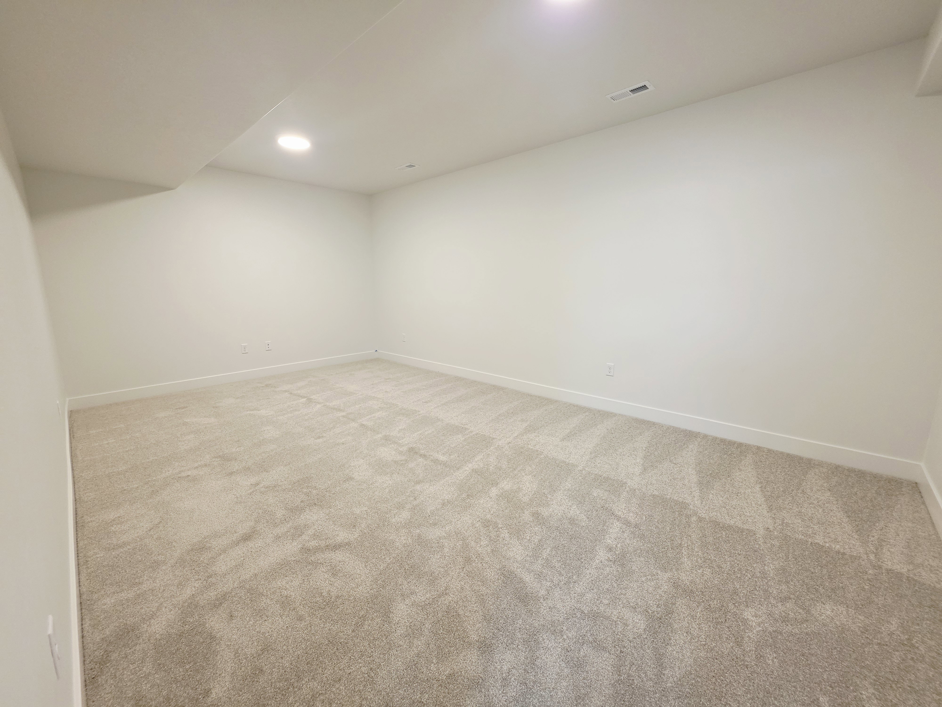 Spacious room featuring light-toned carpeting, recessed ceiling lighting, and crisp white walls with matching baseboards
