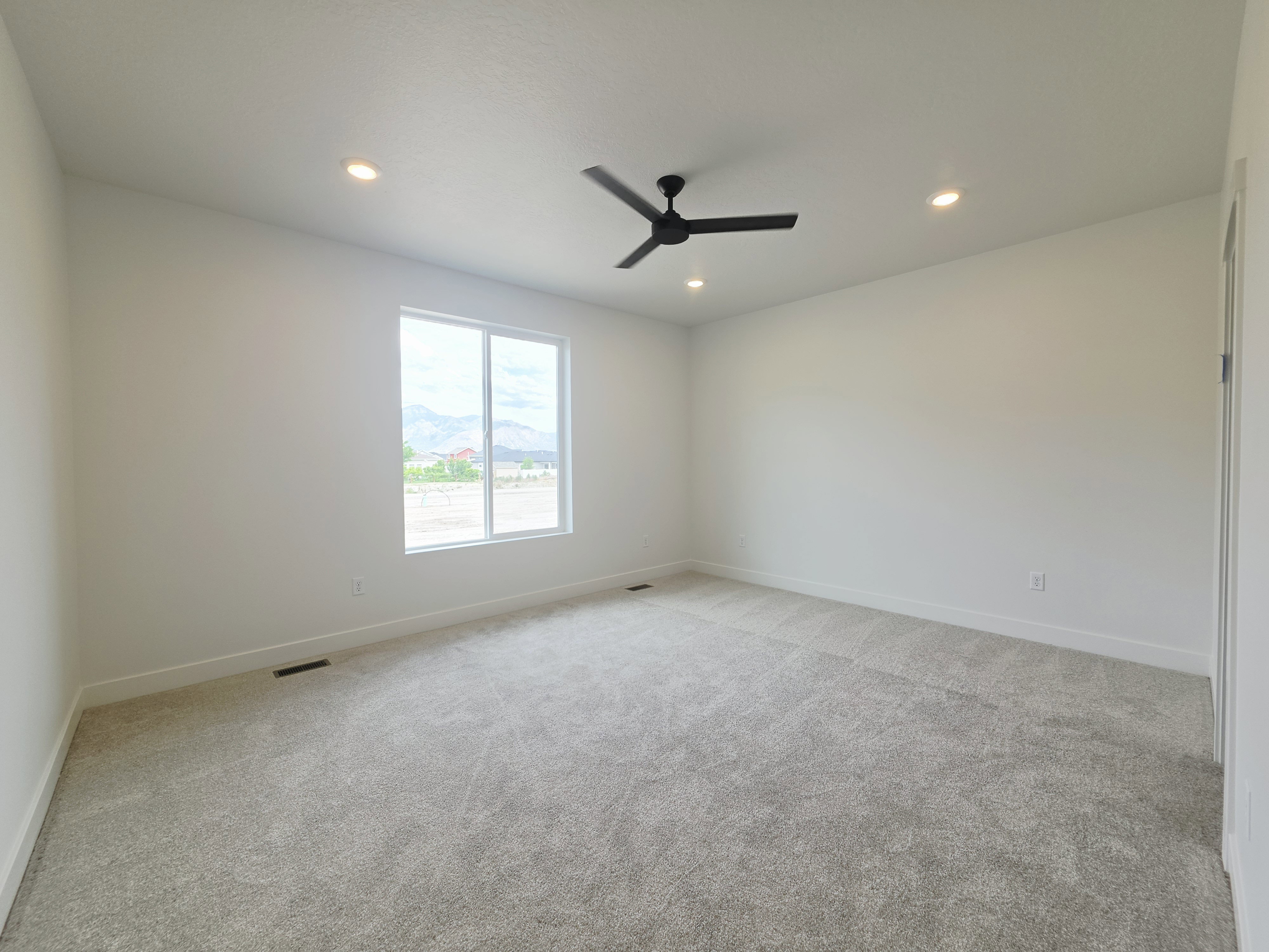 Spacious room featuring light-toned carpeting, a large window, a ceiling fan with matte black blades, and recessed lighting