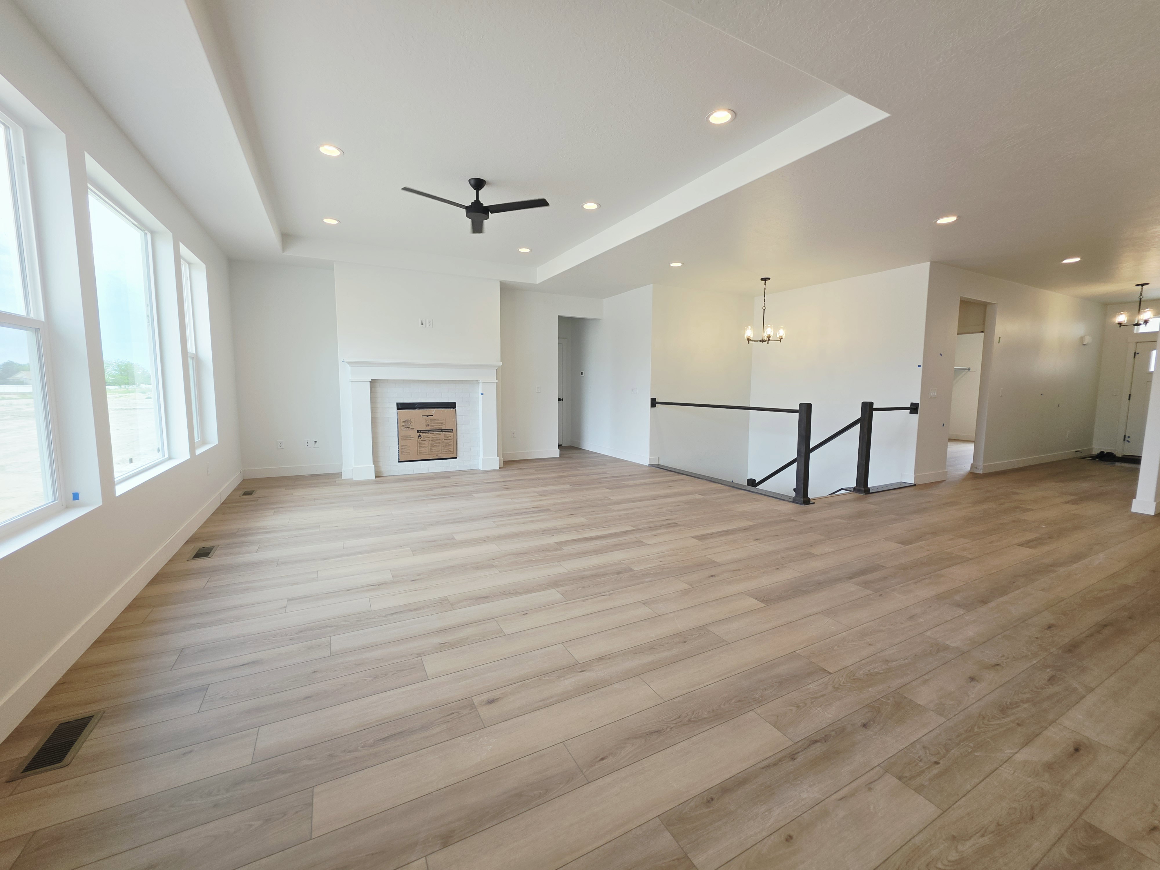 Open-concept living area featuring light wood-finish flooring, a contemporary fireplace with a white mantel, and ample natural light from multiple windows