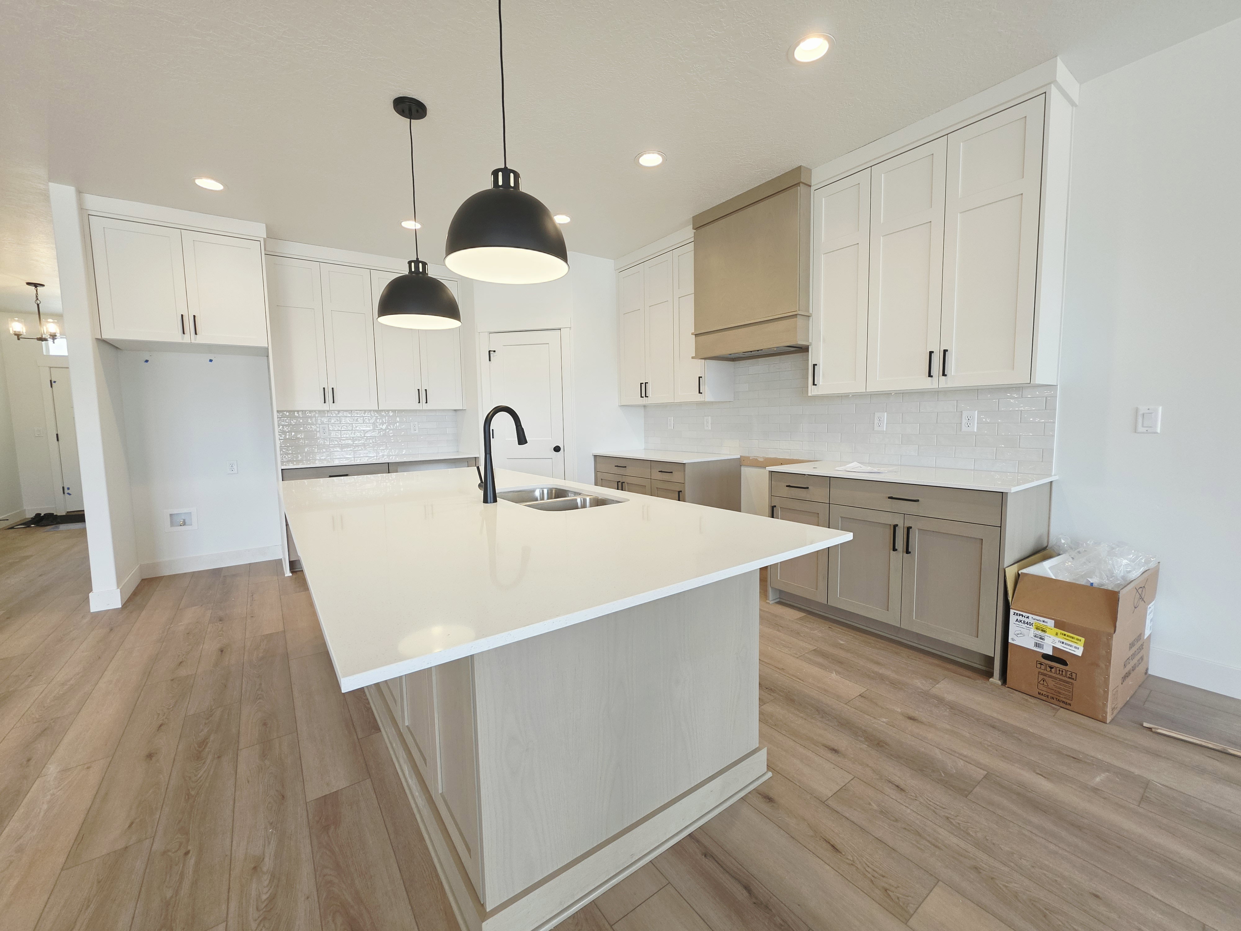 Spacious kitchen featuring a large central island with a sink, quartz countertops, two-tone cabinetry, a tile backsplash, and wood-finish flooring