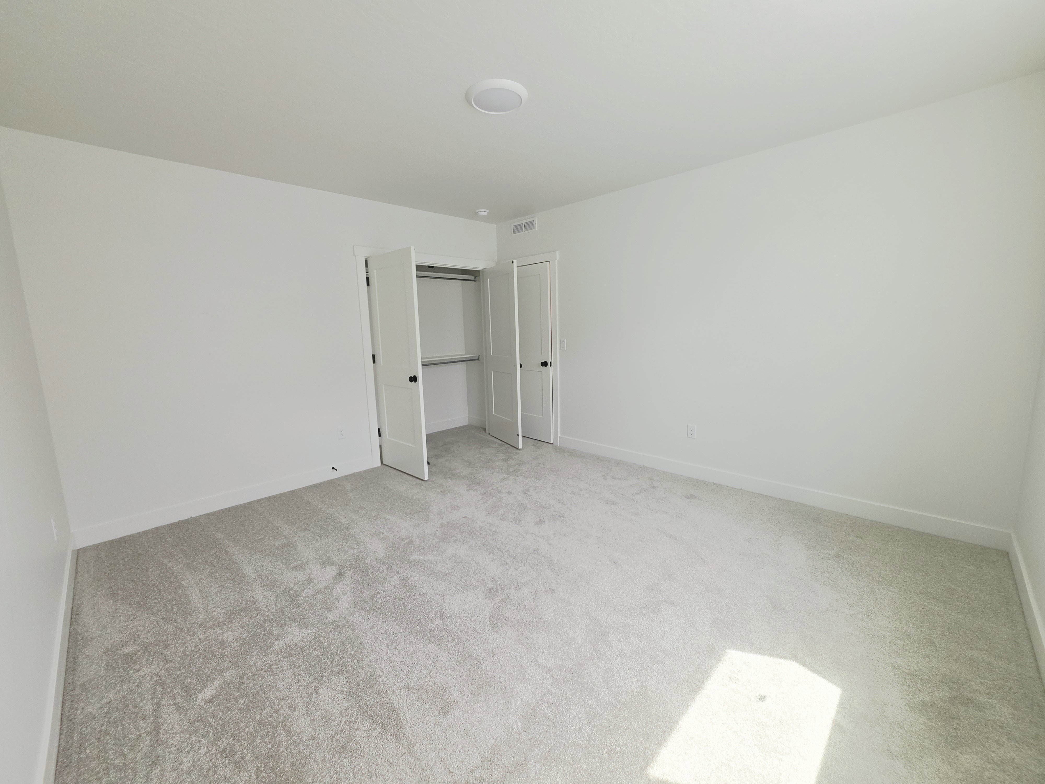 Spacious room featuring light gray carpeting, white walls, and a ceiling-mounted light fixture