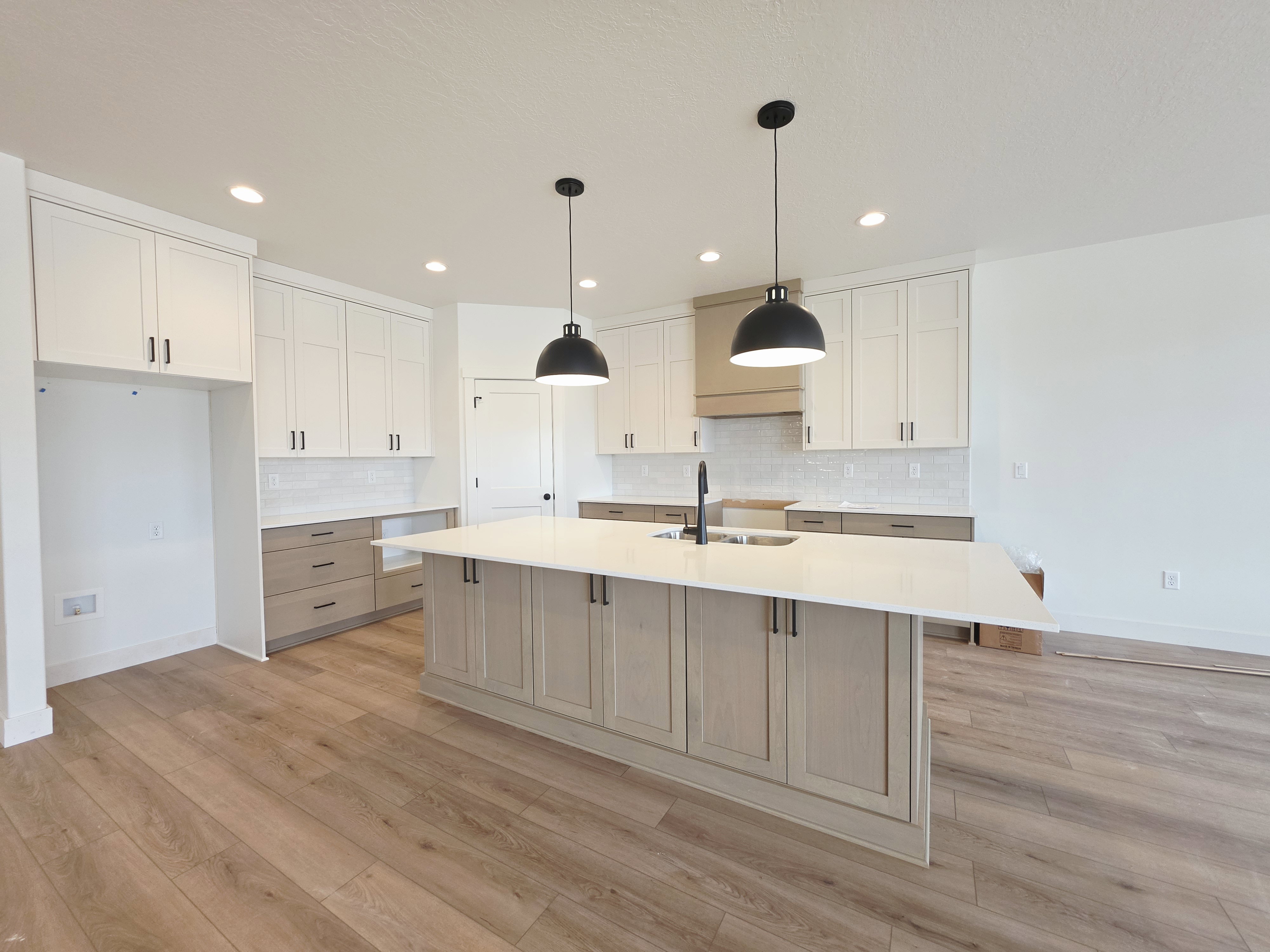 Spacious kitchen featuring an oversized island with a built-in sink, pendant lighting, two-tone cabinetry, wood-finish flooring, and a subway tile backsplash
