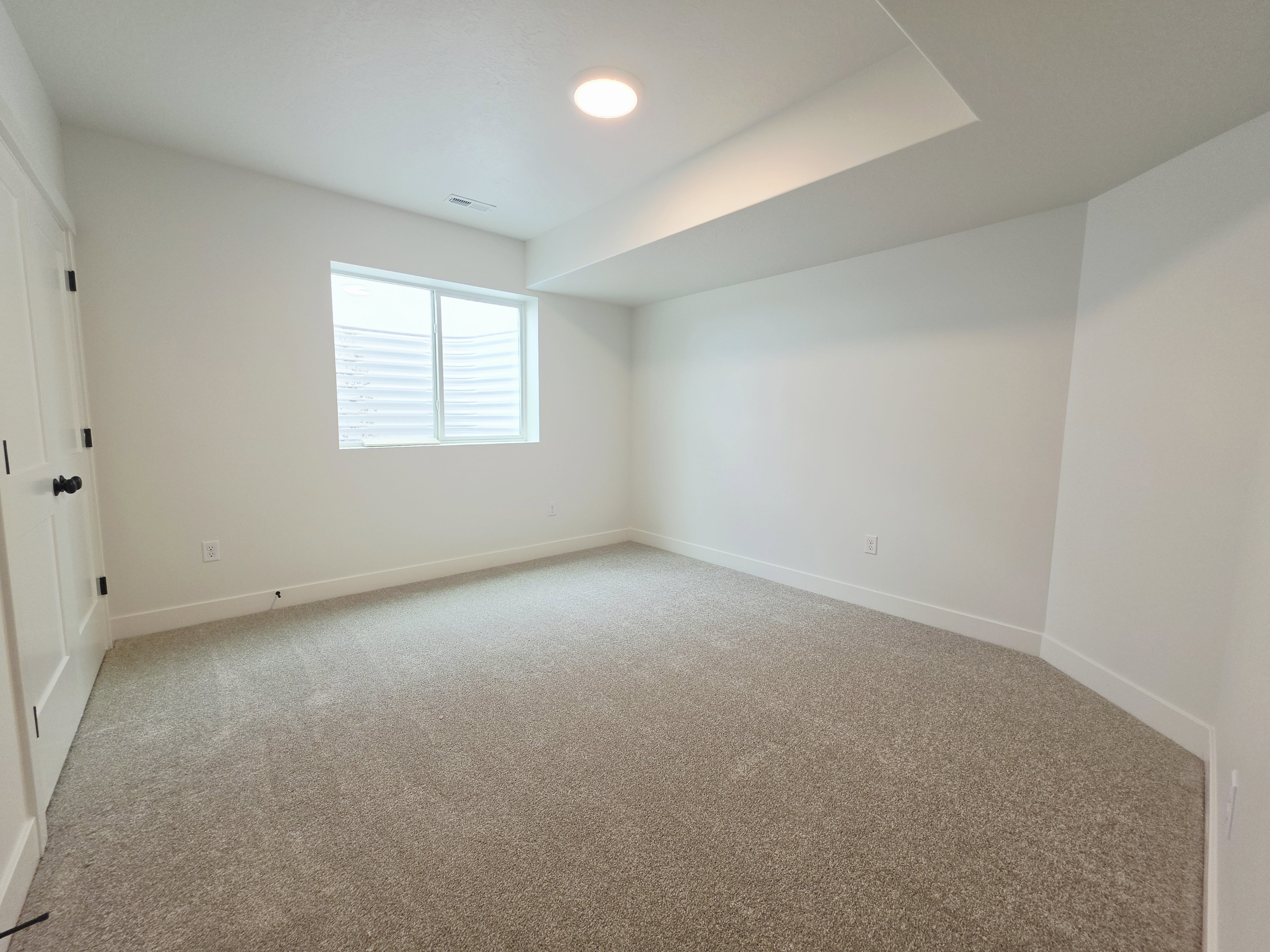 Neutral-toned carpeted room featuring a single window, white walls, and recessed lighting