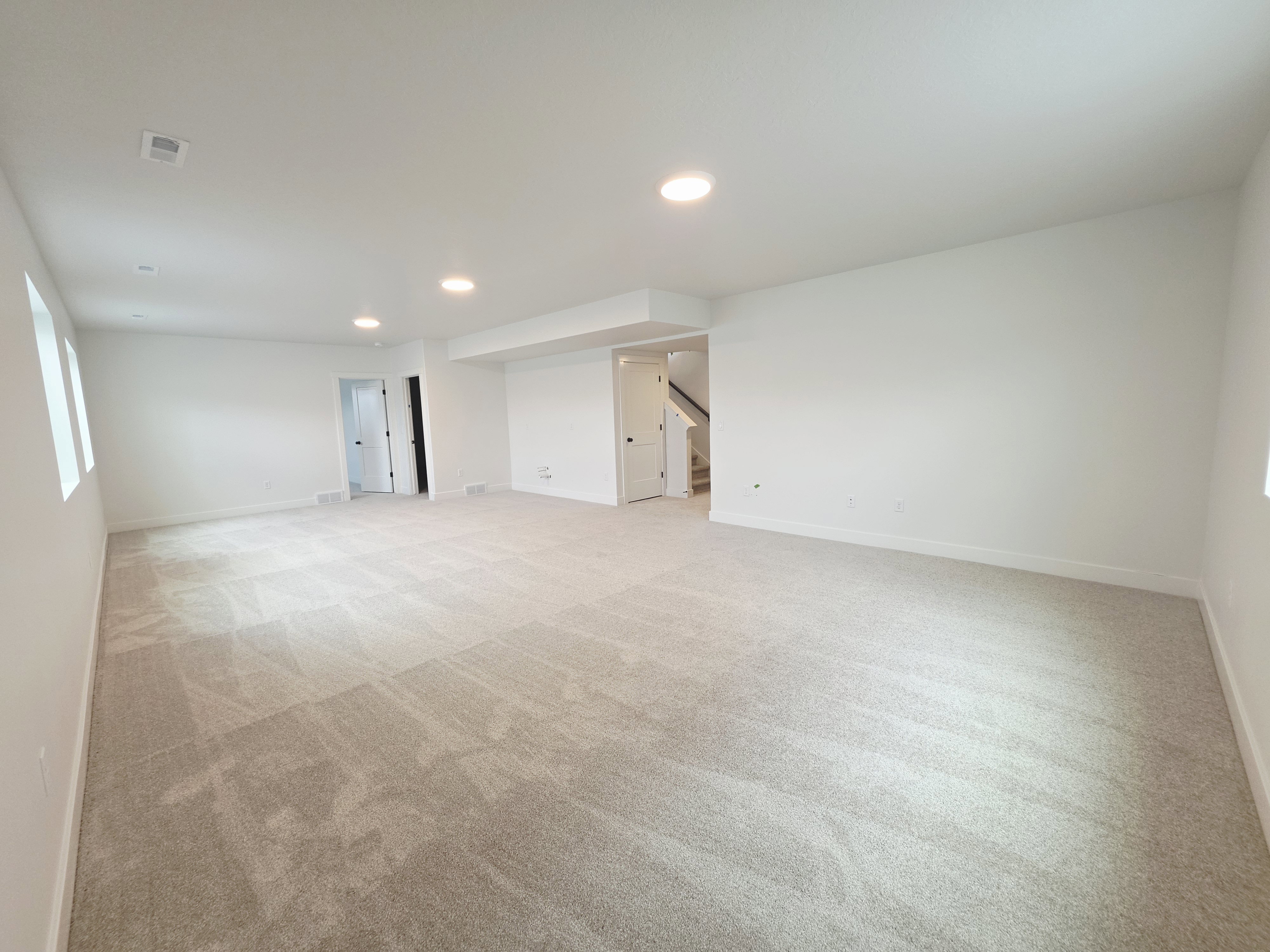 Spacious room featuring light-toned carpeting, white walls, recessed ceiling lighting, and windows providing natural light