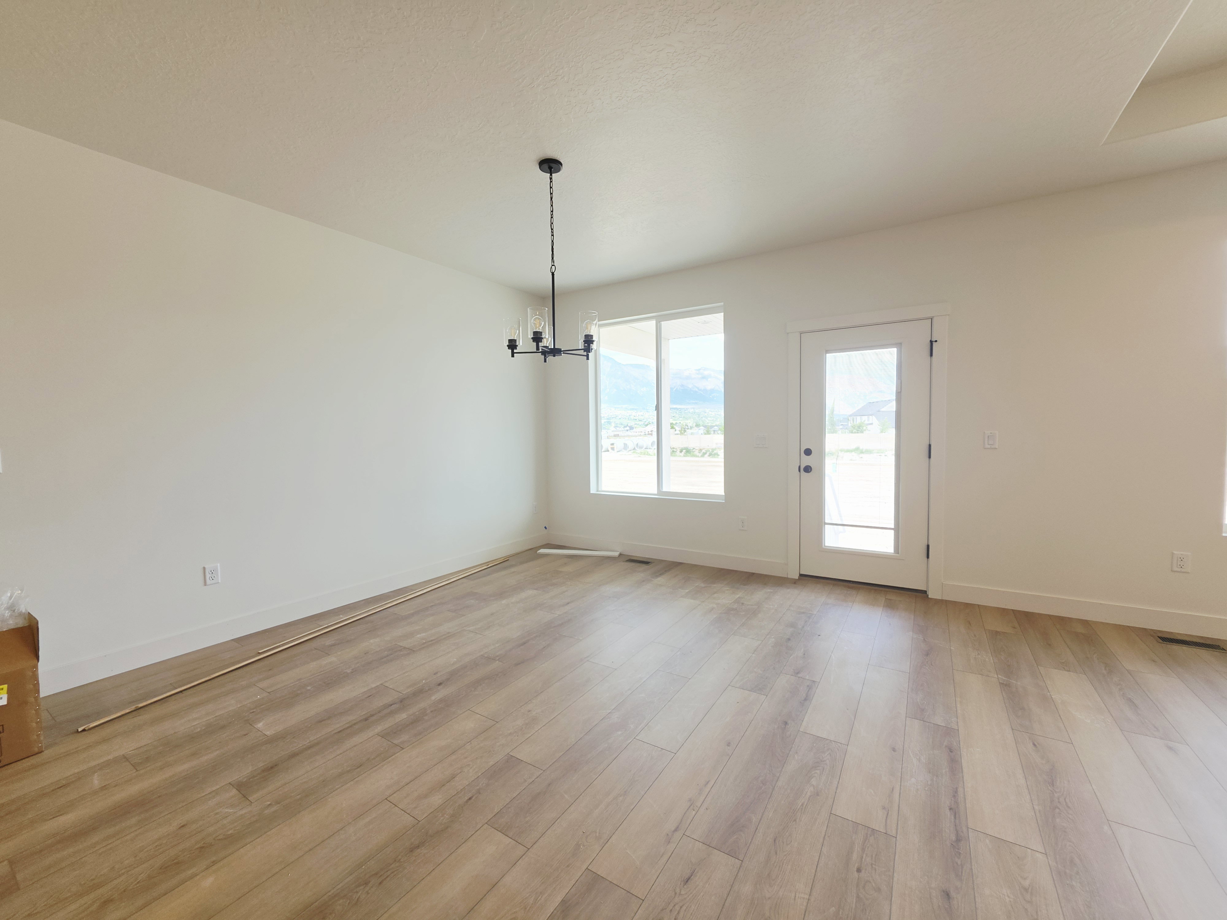 Spacious room featuring wood-finish plank flooring, a contemporary chandelier, large windows with mountain scenery, and a glass-paneled door
