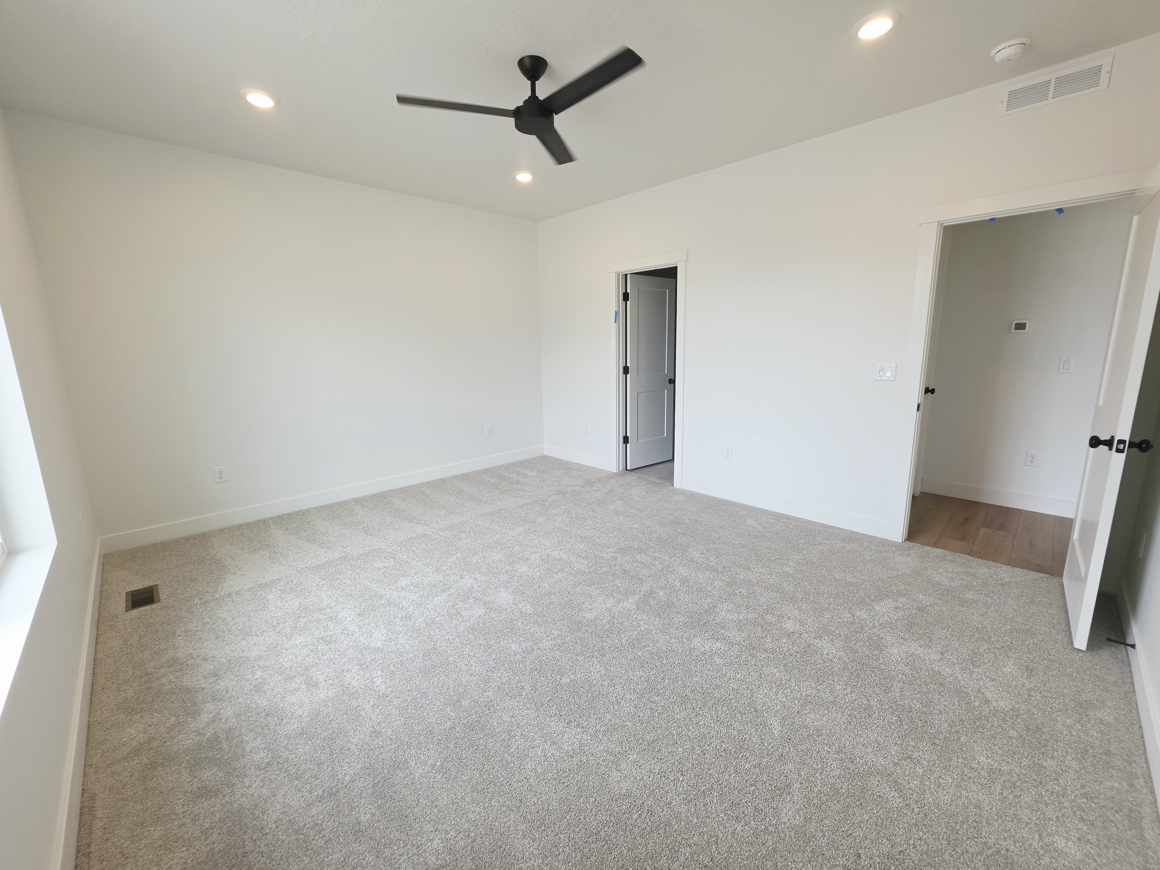 Spacious room featuring light-toned carpet flooring, recessed lighting, and a contemporary black ceiling fan