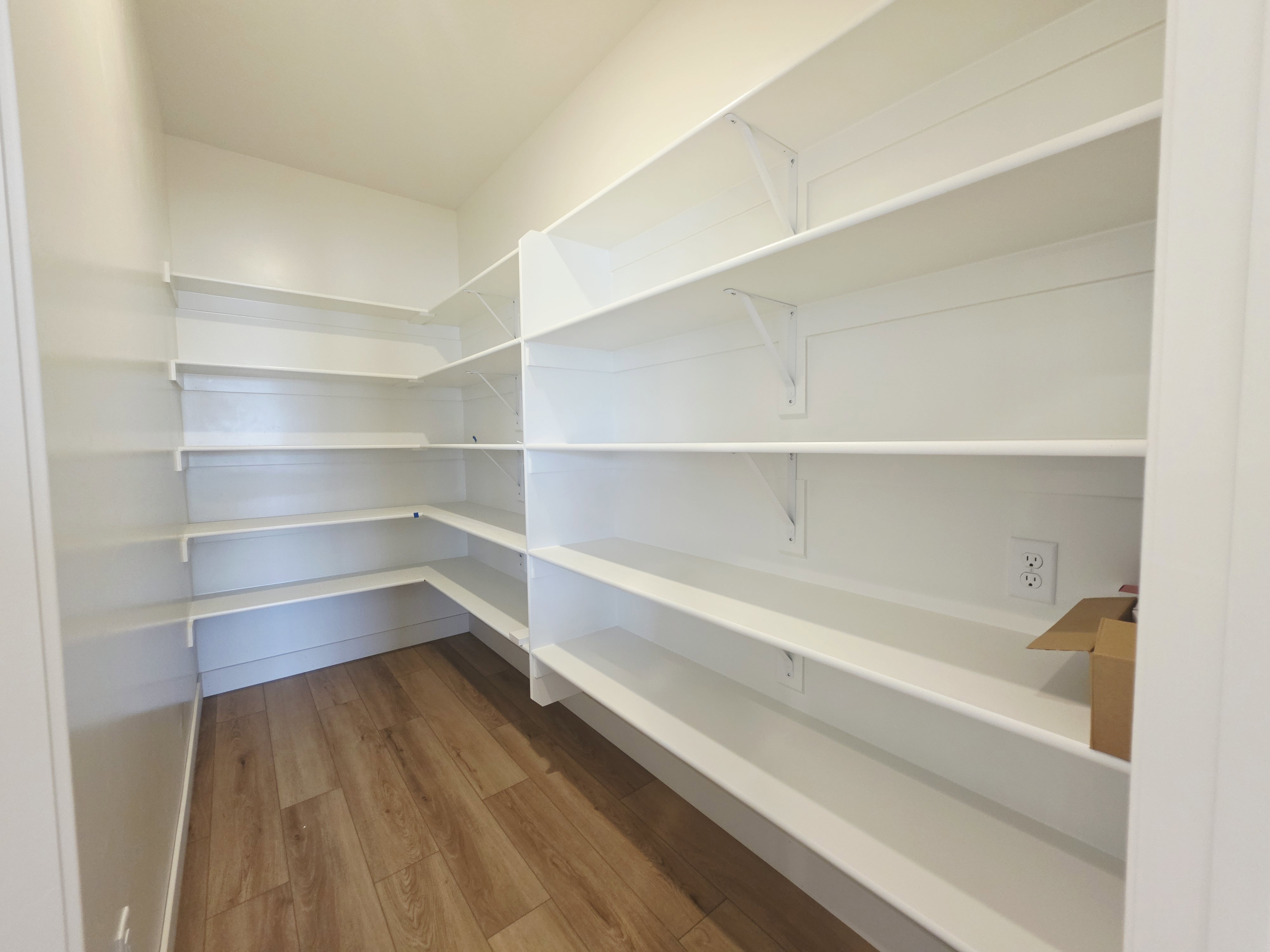 Walk-in pantry featuring extensive white shelving, wood-finish flooring, and a wall outlet
