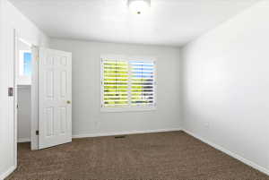 Bright room featuring a window with plantation shutters, neutral-toned carpet flooring, white trim, and a white six-panel door