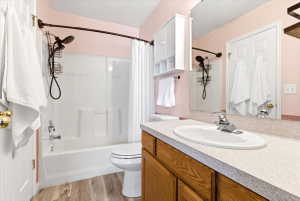 Bathroom with a combination shower and tub, wood-finish vanity, light-toned countertop, integrated sink, and wall-mounted storage cabinet