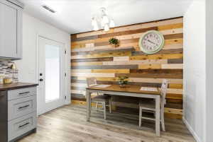 Accent wall featuring varied wood planking, wood-finish flooring, white ceiling, white exterior door with glass insert, and a multi-light ceiling fixture