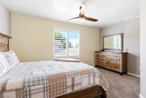 Bedroom featuring carpet flooring, a window with plantation shutters, and a ceiling fan with integrated lighting