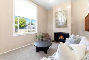 Living area featuring a fireplace with a dark surround, a large window, light-toned walls, and neutral carpet flooring