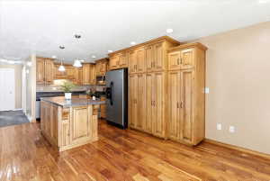 Kitchen featuring extensive wood cabinetry, wood-finish flooring, a central island with a stone-look countertop, a built-in stainless steel refrigerator, and recessed lighting