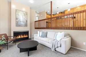 Living area featuring a floor-to-ceiling fireplace with a black surround, vaulted ceiling, and carpeted flooring