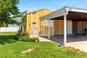Exterior featuring a yellow facade with white trim, a covered carport, and a manicured front lawn