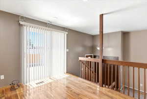 Hardwood flooring extending throughout, featuring a large vertical blind-covered window, and a wood railing system