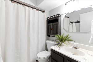 Bathroom featuring a shower with a white textured curtain, a toilet, a wall-mounted dark wood cabinet, a vanity with a white countertop and integrated sink, and a framed mirror with overhead lighting