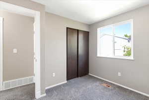 Carpeted room featuring a large window, dark wood-finish bi-fold closet doors, light gray wall paint, and white baseboards