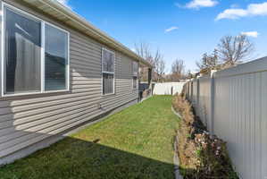 Exterior siding with multiple windows and a level lawn area, bordered by a solid privacy fence and a planted strip