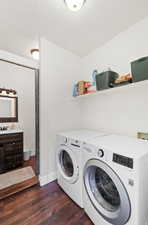 Dedicated laundry area featuring a front-load washer and dryer, a wall-mounted storage shelf, and dark wood-finish flooring