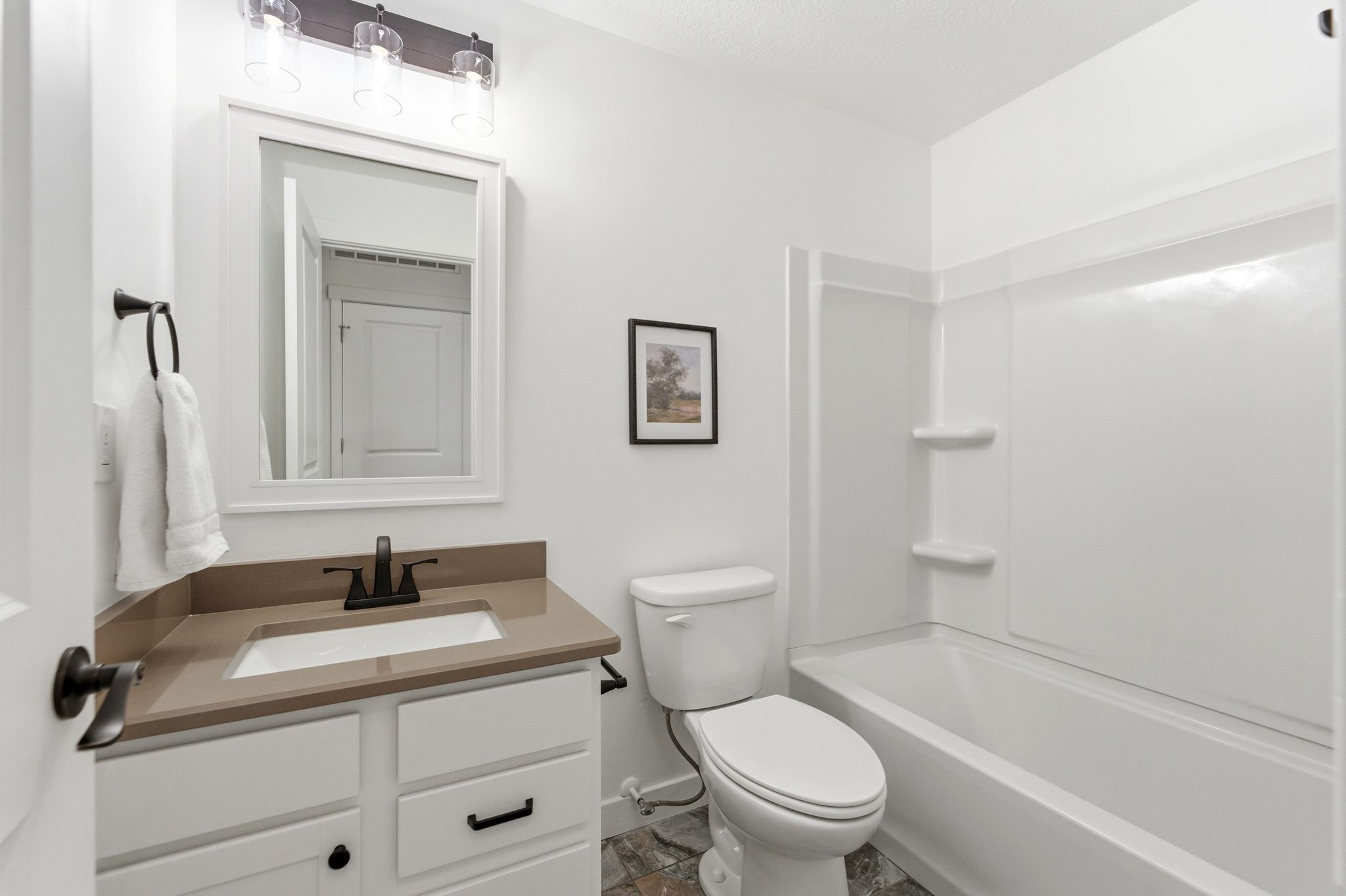 Bright bathroom with white vanity cabinetry, integrated sink, and bronze-finish fixtures