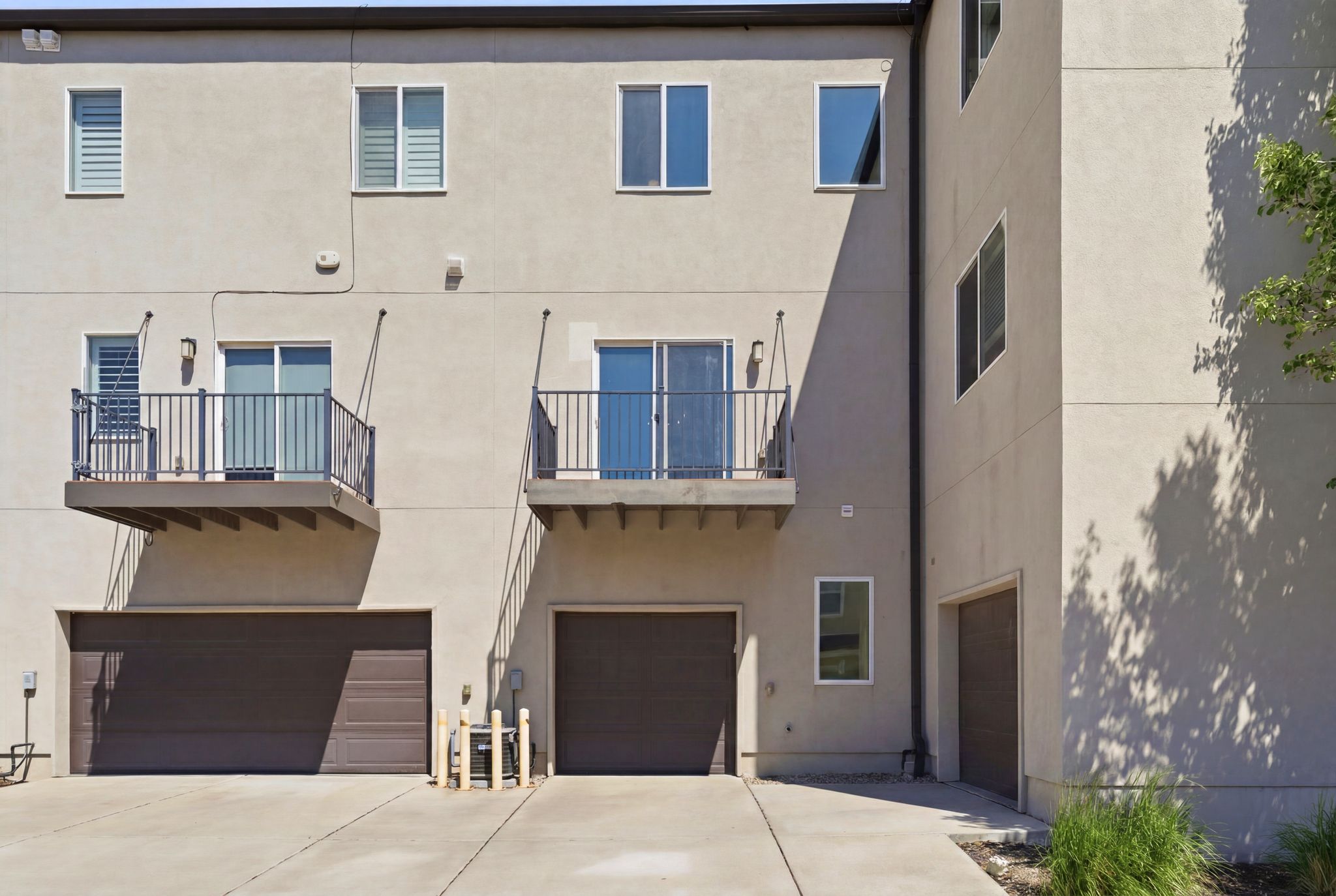 Multi-story stucco exterior featuring two private balconies with metal railings, dual garage doors, and multiple windows with white frames