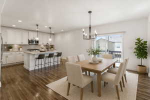 Open-concept living space with wood-finish flooring, a contemporary dining area, and a kitchen featuring white cabinetry, an island with seating, and stainless steel appliances