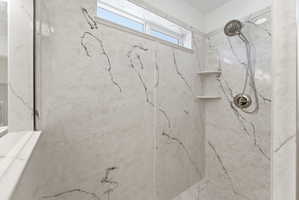 Shower stall featuring large-format wall panels with black veining, a multi-function showerhead, and integrated corner shelving