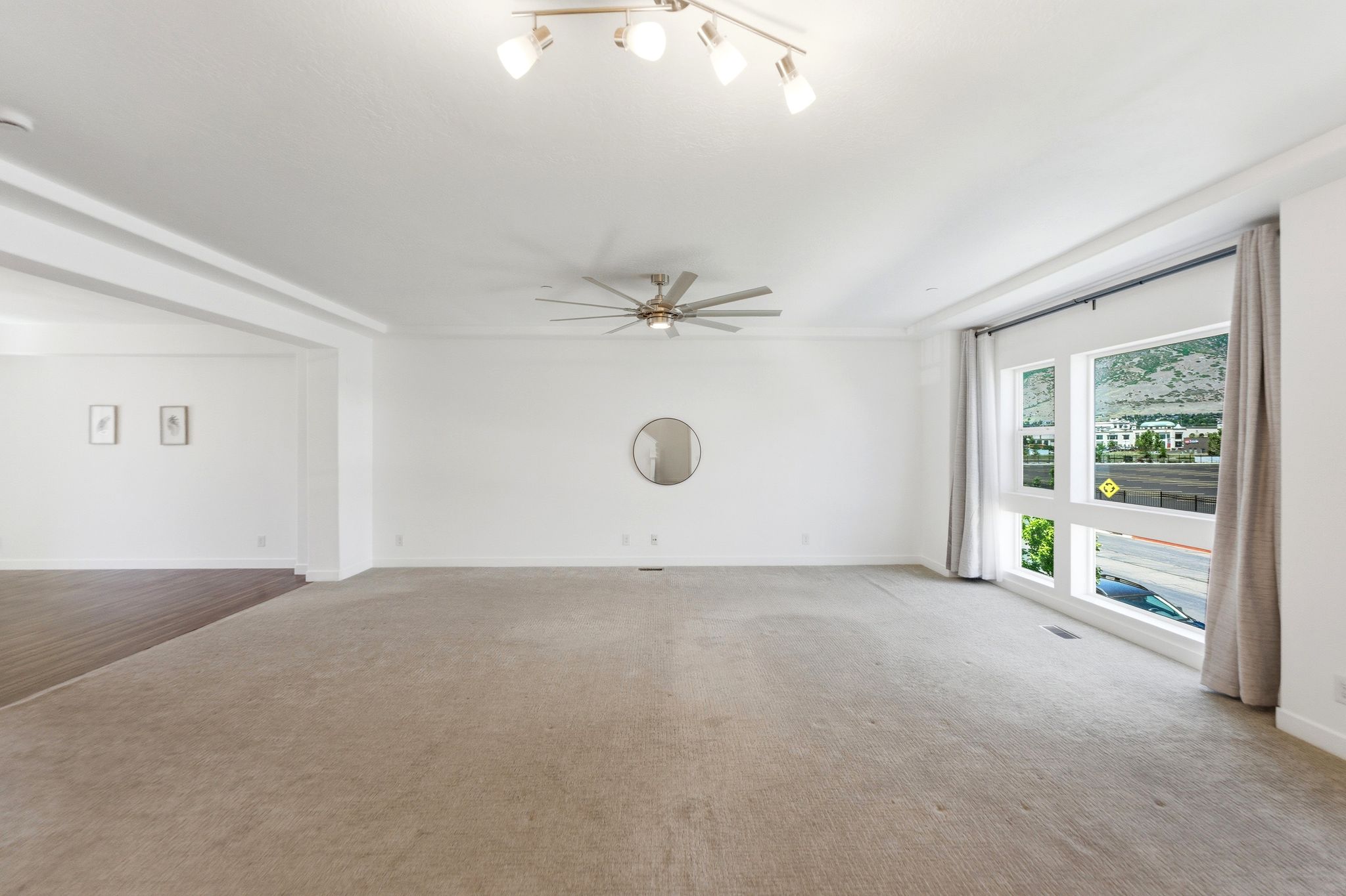 Spacious living area featuring carpet flooring, large windows, recessed ceiling details, a ceiling fan, and track lighting