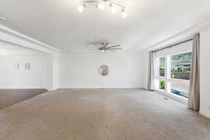 Spacious living area featuring carpet flooring, large windows, recessed ceiling details, a ceiling fan, and track lighting