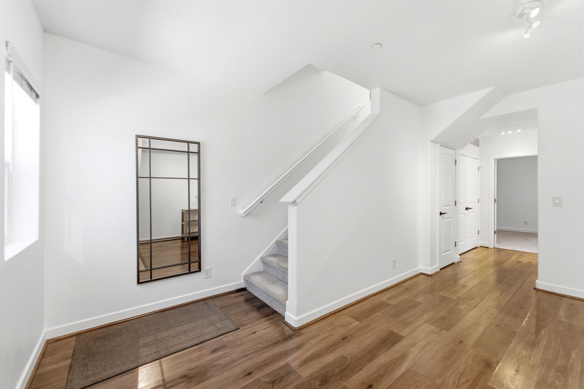 Entryway featuring wood-finish flooring, white walls, and a carpeted staircase with a white handrail