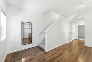Entryway featuring wood-finish flooring, white walls, and a carpeted staircase with a white handrail