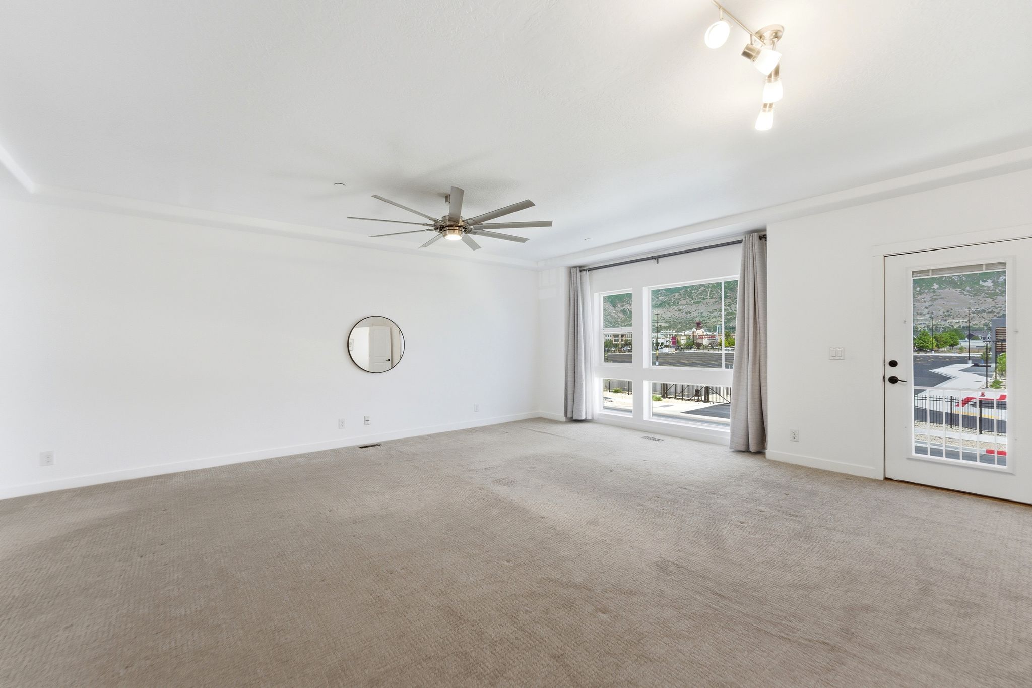 Spacious room featuring neutral carpet flooring, large multi-pane windows, a glass-panel door, contemporary ceiling fan, and decorative crown molding