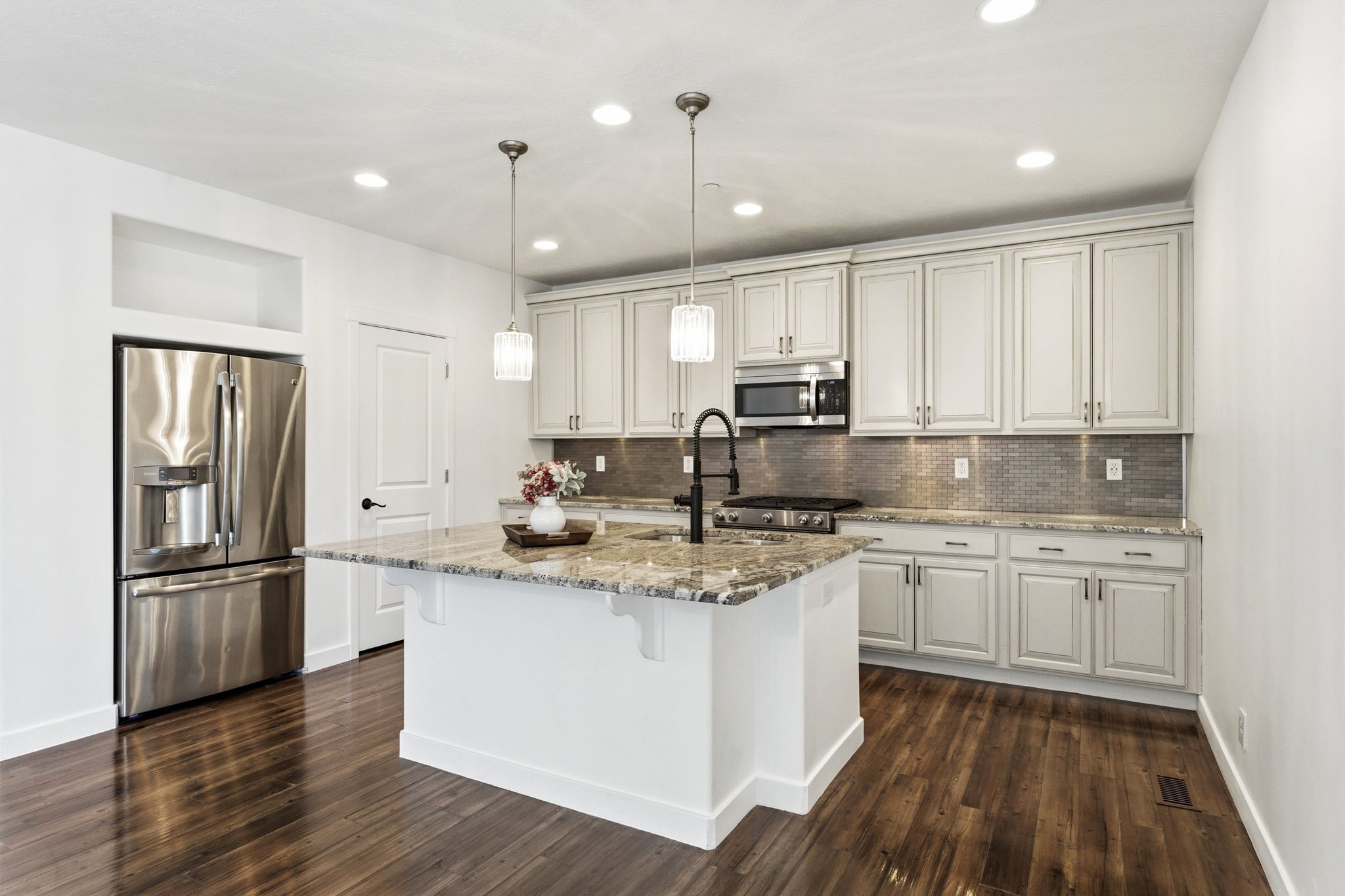 Kitchen featuring a central island with a multi-toned countertop, stainless steel appliances, white cabinetry with dark hardware, a mosaic tile backsplash, and wood-finish flooring