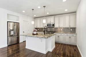 Kitchen featuring a central island with a multi-toned countertop, stainless steel appliances, white cabinetry with dark hardware, a mosaic tile backsplash, and wood-finish flooring