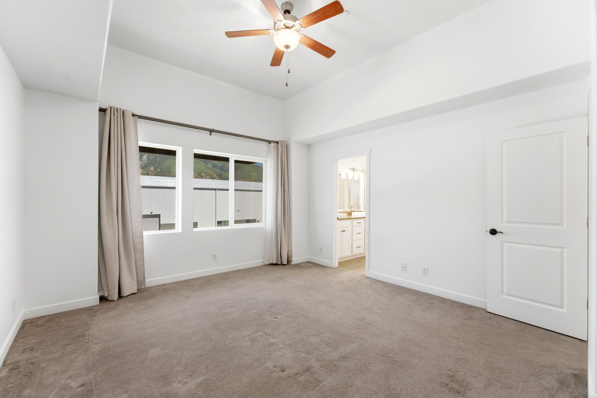 Spacious room featuring vaulted ceilings, a wood-finish ceiling fan, and large windows with opaque drapery