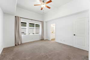Spacious room featuring vaulted ceilings, a wood-finish ceiling fan, and large windows with opaque drapery