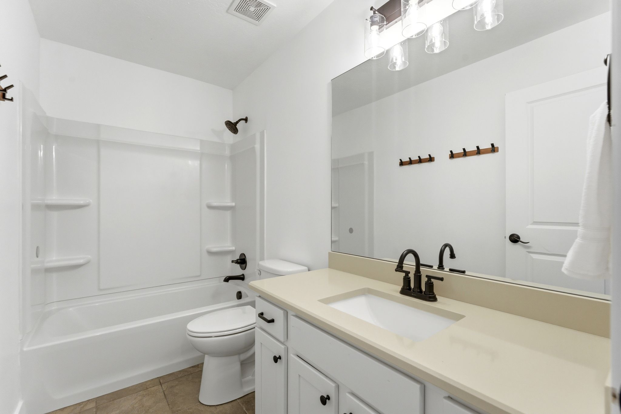Full bathroom featuring a white tub/shower combination with integrated shelving, a white toilet, and a vanity with a light-toned countertop, integrated sink, and dark bronze-finish fixtures