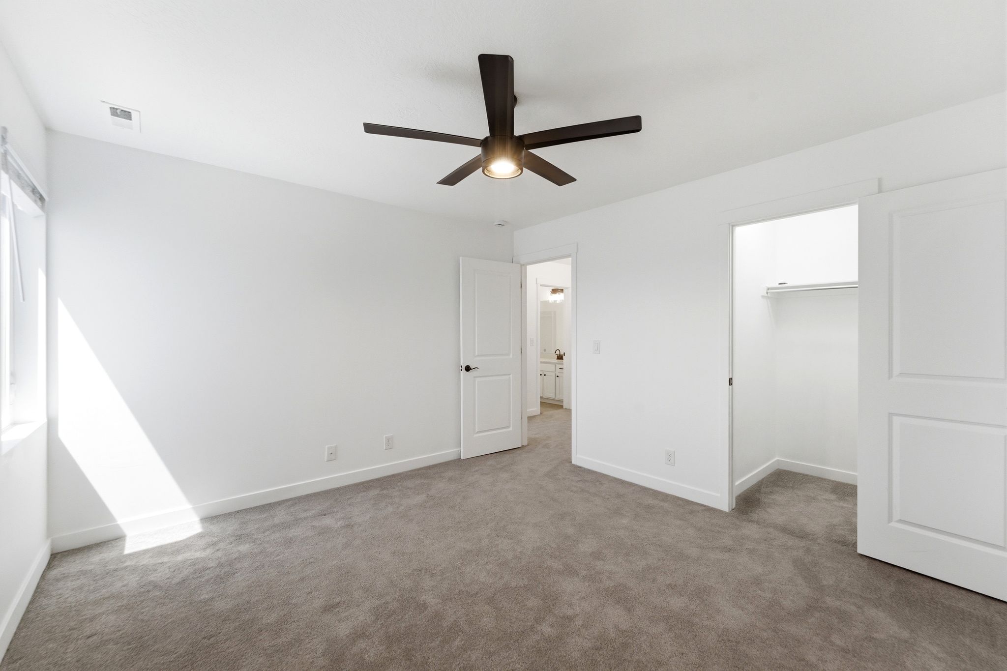 Neutral carpeted room with a modern ceiling fan, white walls, and a window