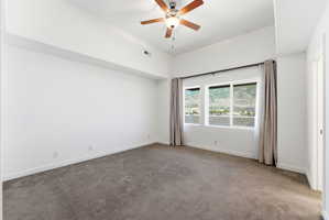 Spacious room with plush carpet flooring, a large window offering a mountain backdrop, a ceiling fan, and high ceilings