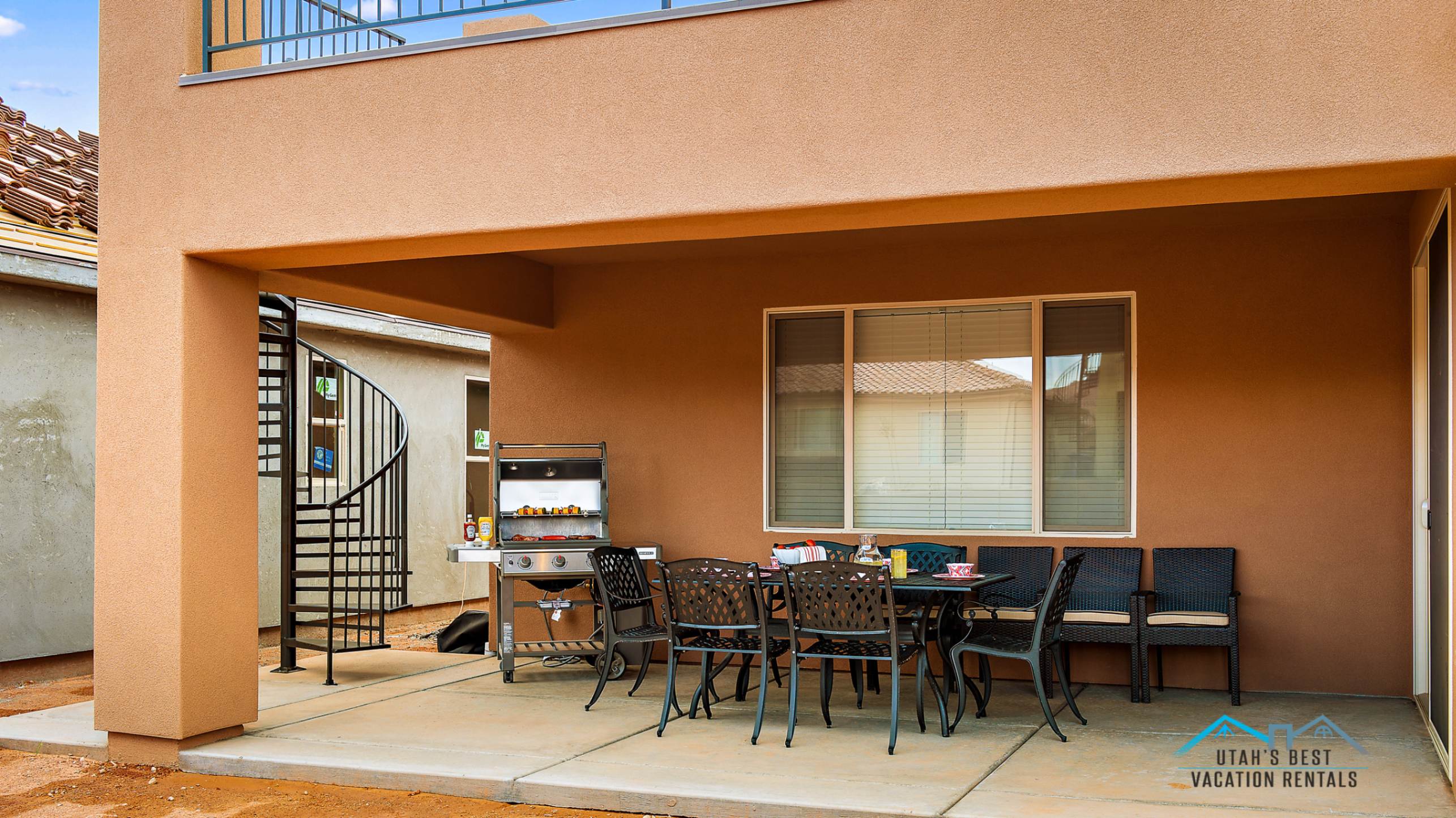 Covered patio featuring concrete flooring and a spiral staircase providing exterior access to an upper-level balcony with metal railing