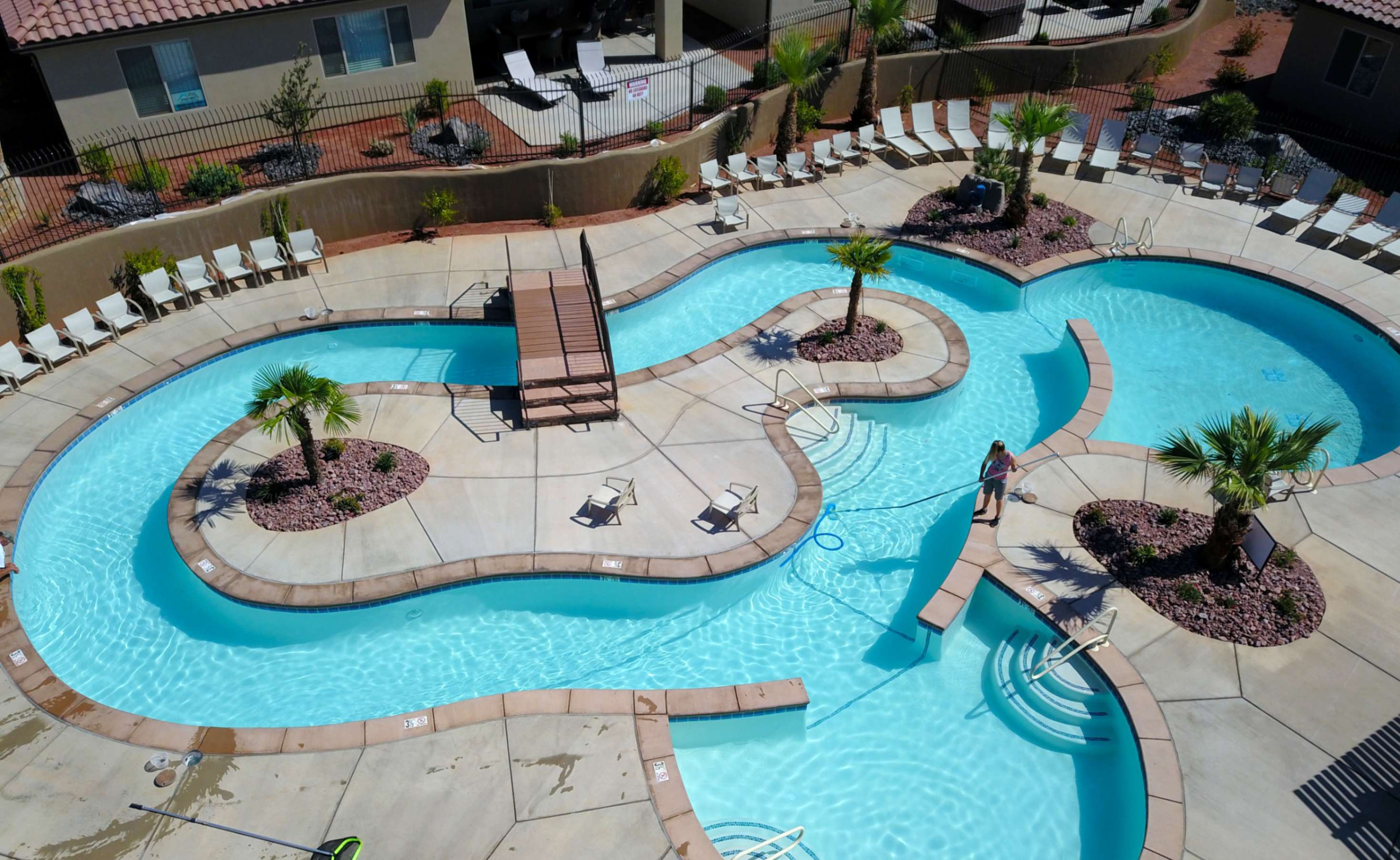 Expansive community pool area featuring a meandering lazy river, multiple swimming zones, and a wooden pedestrian bridge
