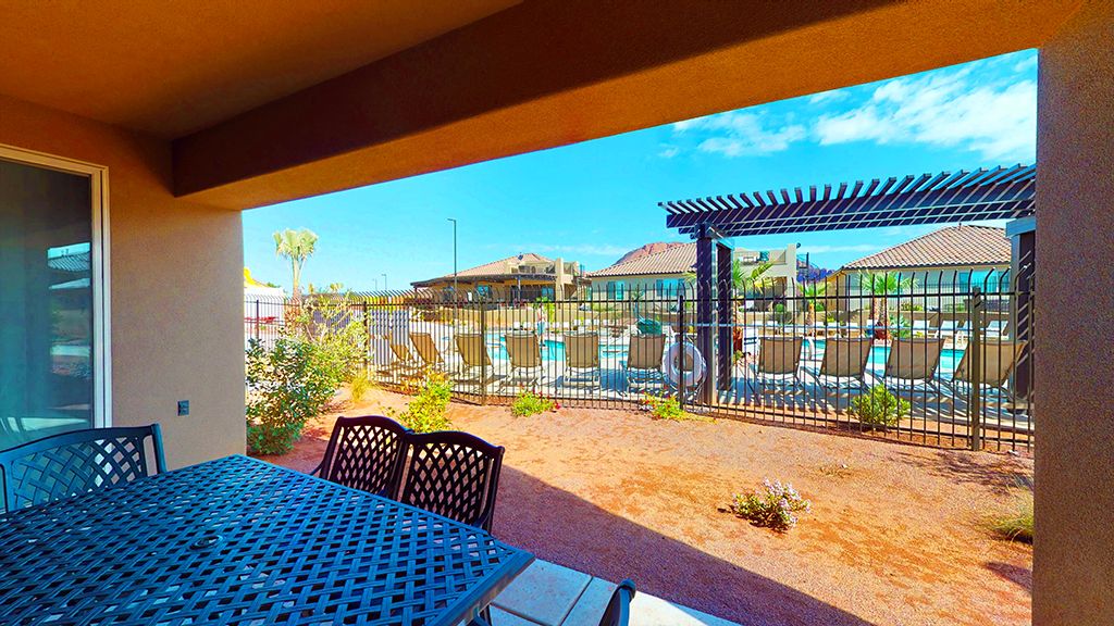 Covered patio area with direct access to a community pool, featuring a metal perimeter fence and an overhead pergola
