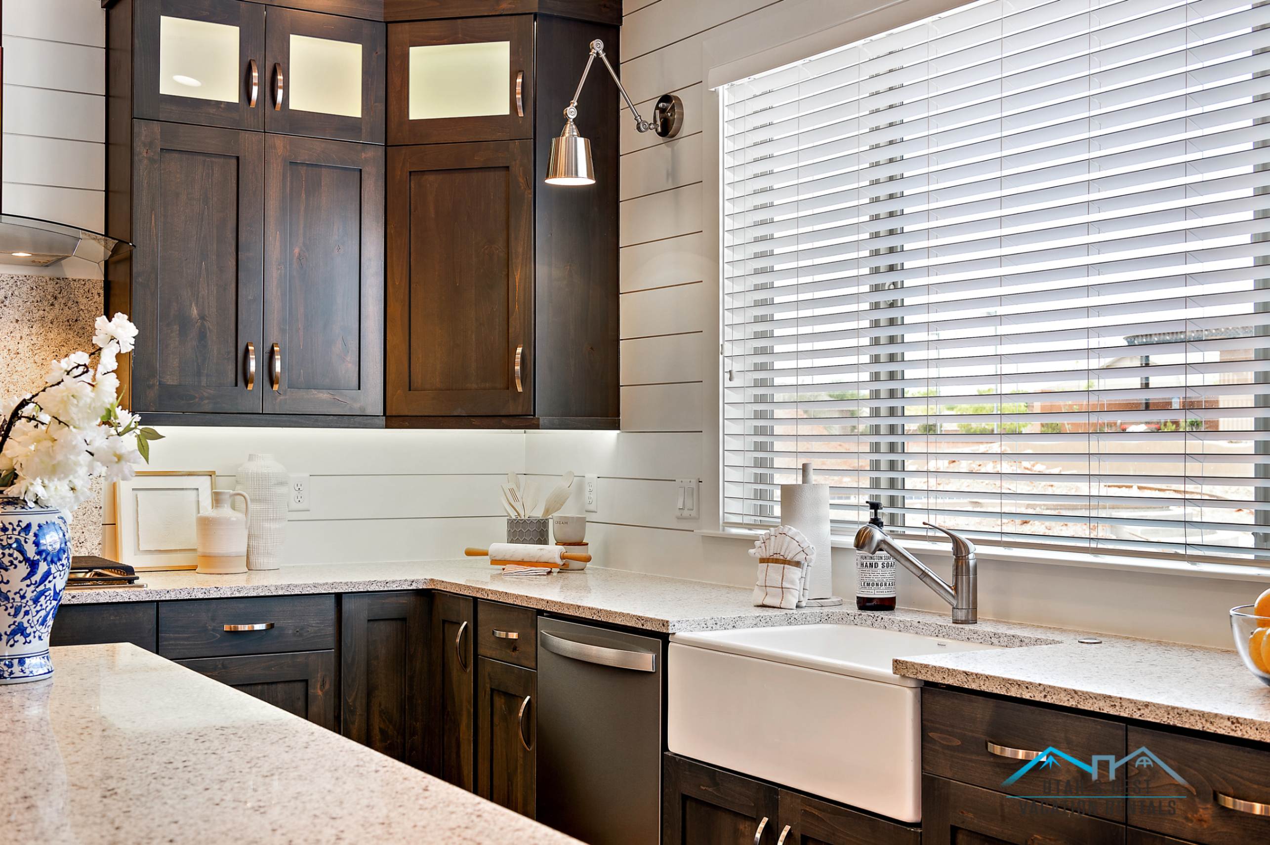 Kitchen featuring dark wood cabinetry, light speckled countertops, a white farmhouse sink, and a stainless steel faucet