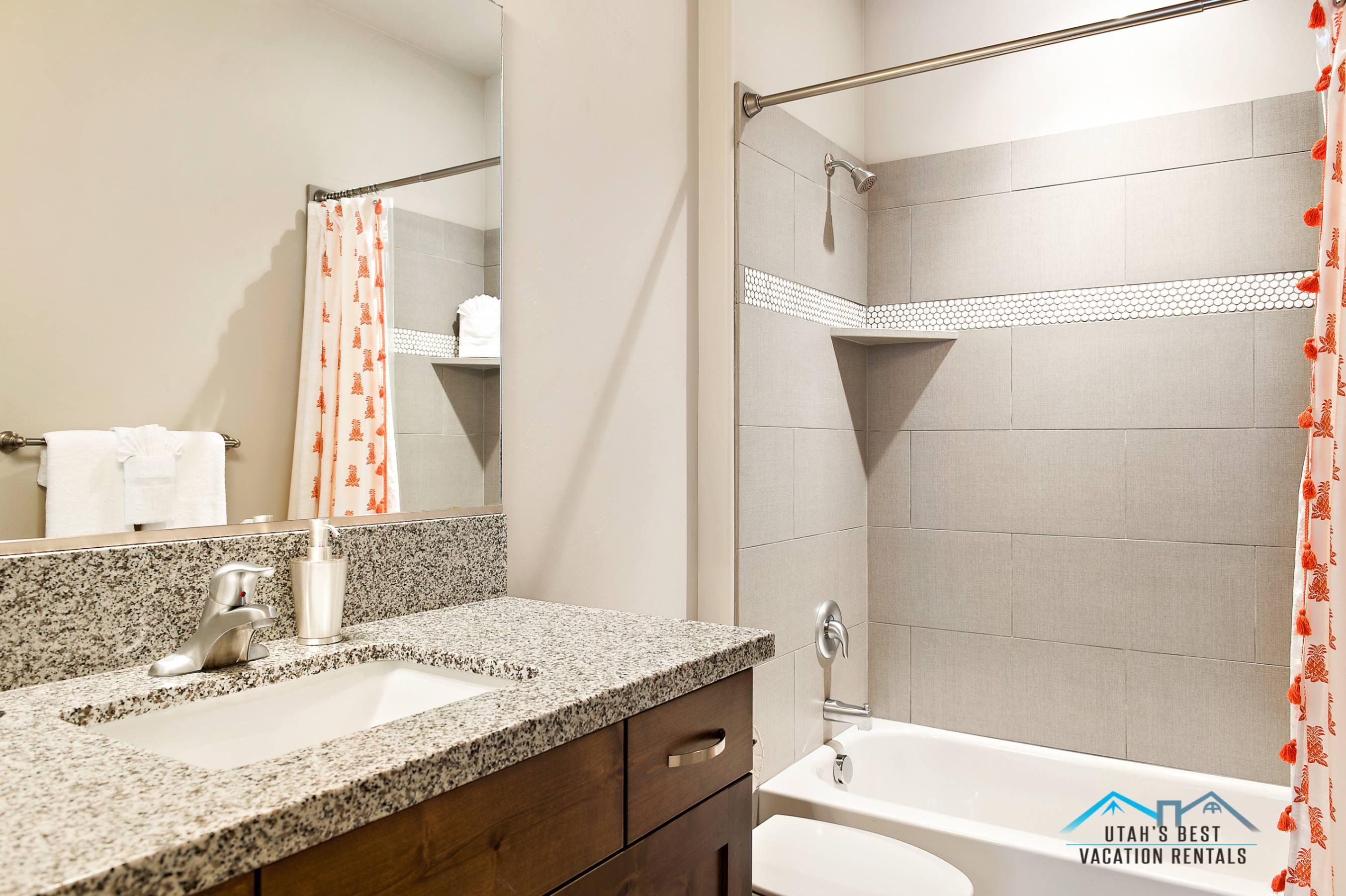 Bathroom featuring a built-in tub and shower combination with light-toned rectangular tile surround and a decorative mosaic accent strip