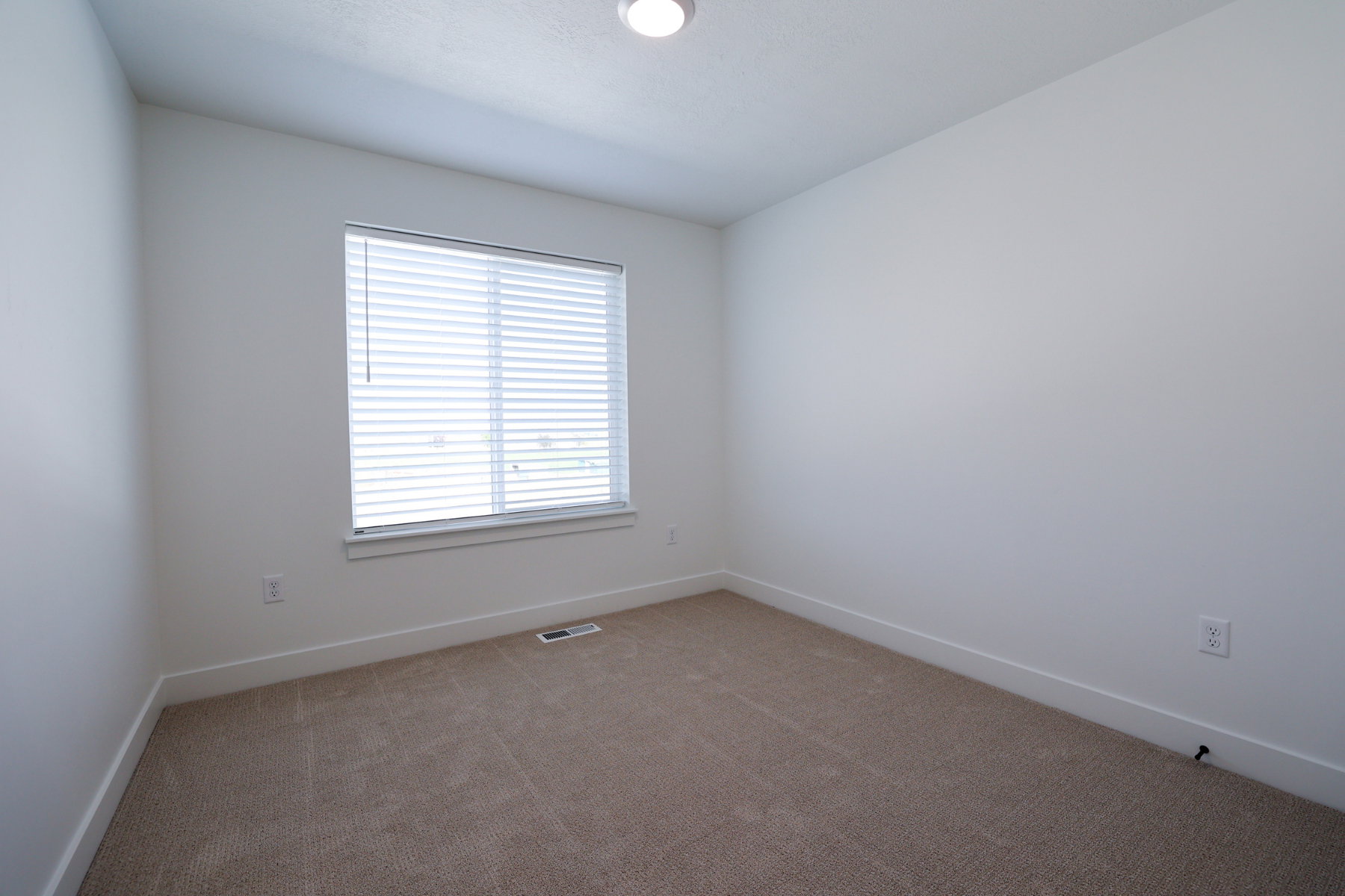 Room with light tan carpeting, white baseboards, and a single window featuring horizontal blinds