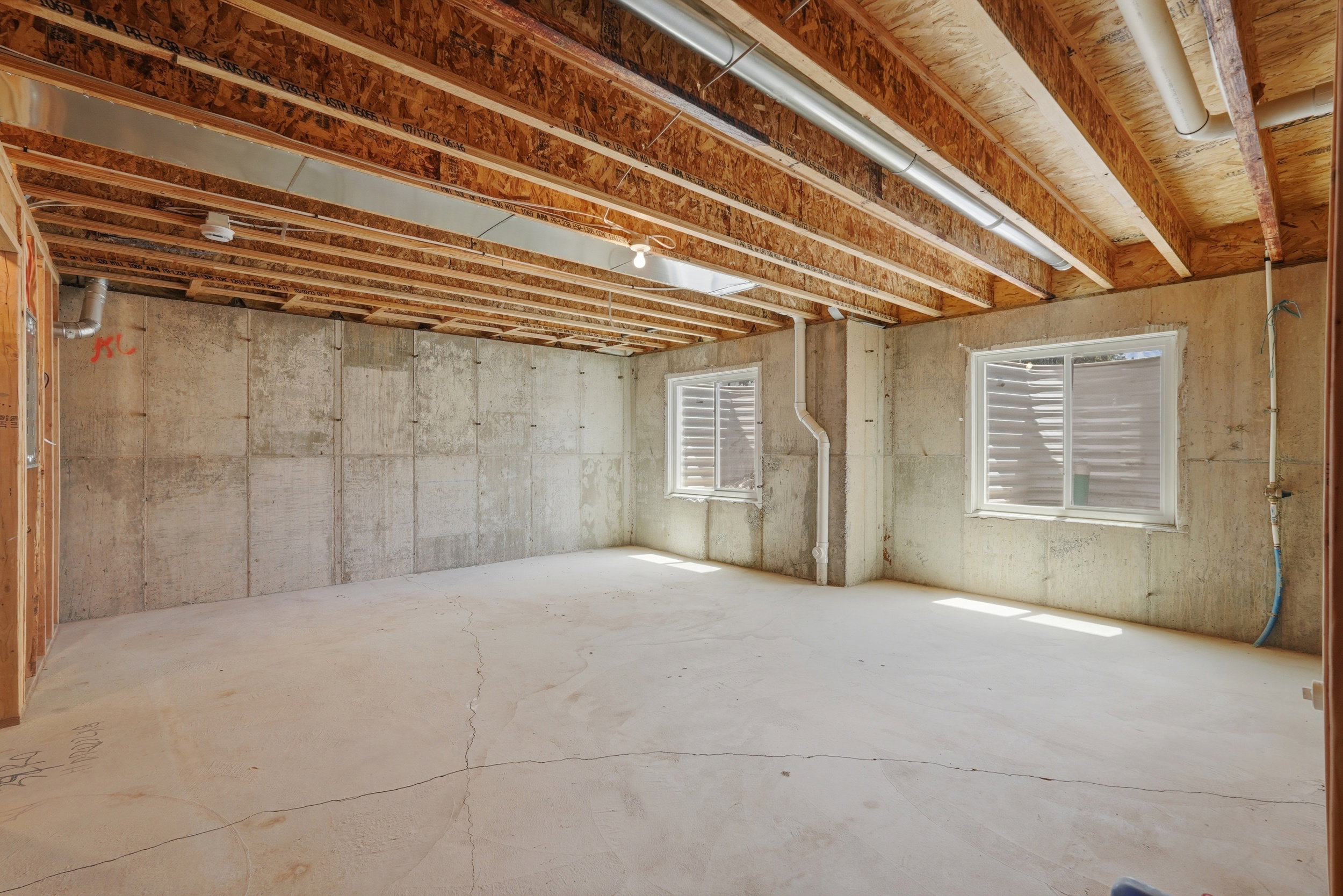 Unfinished basement featuring exposed wood joists and concrete walls, with two windows providing natural illumination