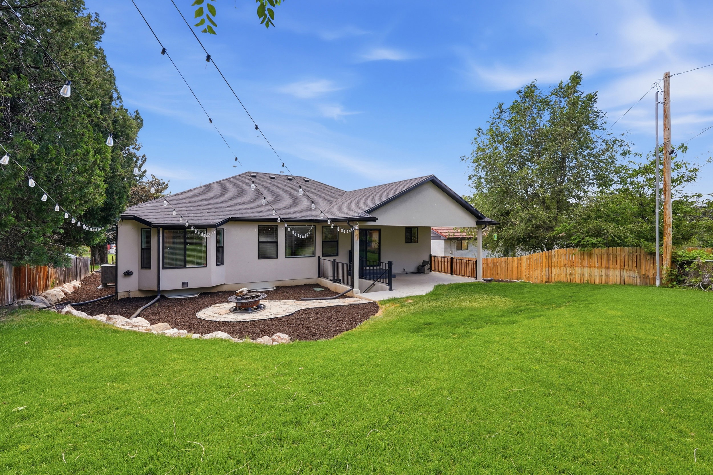 Expansive green lawn with a wood fence, fire pit and covered patio